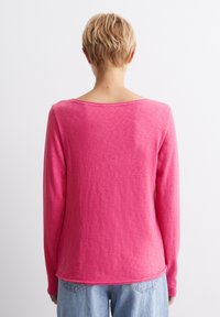 Långärmad rosa skjorta, mjukt tyg, rund halsringning och rundad nederkant. Bakifrån visas en avslappnad passform och subtil textur. Kombinerad med ljusblå jeans.