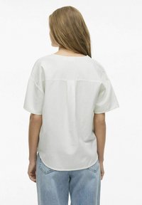 Weißes Baumwoll-T-Shirt, lockere Passform, kurze Ärmel, leicht abgerundeter Saum, Rückennaht-Detail, kombiniert mit hellblauen Jeans.