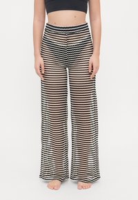 Pantaloni a gamba larga a righe bianche e nere con un design ondulato, caratterizzati da una texture trasparente e una vita alta.