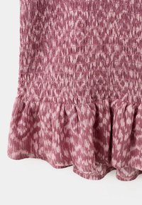 Gros plan sur un tissu rose avec une partie supérieure smockée et un ourlet à volants présentant un motif abstrait léger.