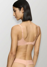 Reggiseno rosa chiaro con spalline regolabili, texture liscia e chiusura a gancio sul retro. Design semplice, hardware minimale, senza decorazioni.