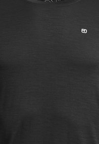 Close-up of dark textured fabric with small white "RJ" logo near neckline.