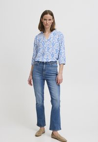 Blusa azzurra a fantasia con scollatura a V, maniche a tre quarti. Abbinata a jeans chiari a zampa d'elefante e scarpe flat color beige.
