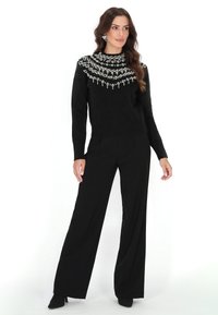 Pulover negru cu guler înalt, care prezintă detalii elaborate cu mărgele albe pe umeri. Asortat cu pantaloni negri cu picioare largi.