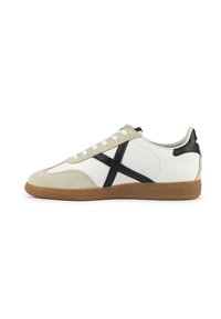White and beige sneaker with black accents, suede and leather material, lace-up design, rubber sole with a textured gum outsole.