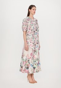 Floral blouse with puff sleeves in pastel colors, paired with a cream-colored skirt featuring a colorful floral pattern. Heeled sandals complete the look.