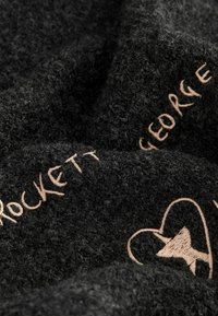 Schwarzer, strukturiert Stoff mit einem flauschigen Aussehen, verziert mit hellbraunem, gesticktem Text und Designs, die einen kontrastierenden Akzent setzen.