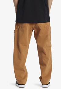 Pantalones cargo color beige con un ajuste suelto, que cuentan con dos bolsillos laterales y solapas traseras, fabricados con material de algodón duradero.