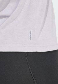 T-shirt de sport gris clair avec une texture douce, arborant un petit logo "AEROREADY" près de l'ourlet, associé à des leggings noirs.