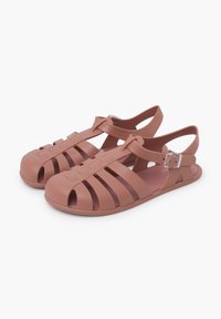Pink rubber sandals with multiple horizontal and vertical cutouts, closed toe, adjustable buckle strap at the ankle, smooth texture.