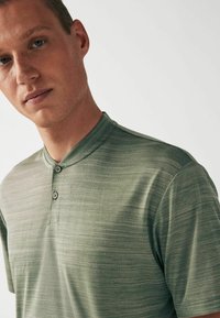 Kortærmet polo shirt i lysegrøn med et struktureret stribet mønster, en mandarin krave og to knapper ved halsen.