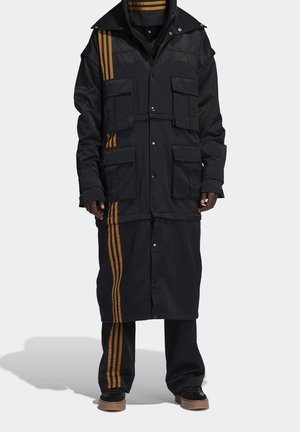Czarna kurtka z złotymi paskami, licznymi kieszeniami, zapięciami na zatrzaski i warstwowym krojem. Posiada długą sylwetkę i pasujące spodnie.