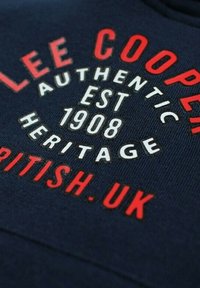 Sweat-shirt bleu marine avec texte circulaire rouge et blanc. Présente le nom de la marque, "Lee Cooper", et la date de création, 1908, embossés sur le tissu.