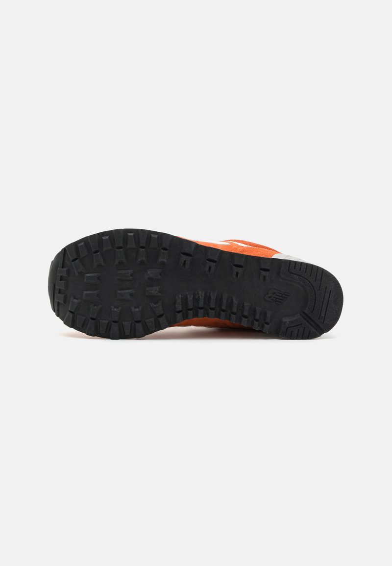 Baskets orange avec une semelle en caoutchouc noir texturé, présentant des rainures profondes pour une meilleure traction, un embout arrondi et un logo de marque blanc contrastant.