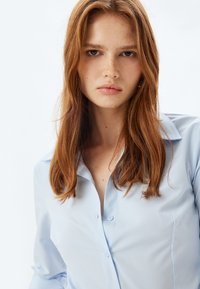 Camicia button-up azzurro chiaro con colletto, caratterizzata da una texture liscia e sottili righe verticali, progettata con una silhouette aderente.