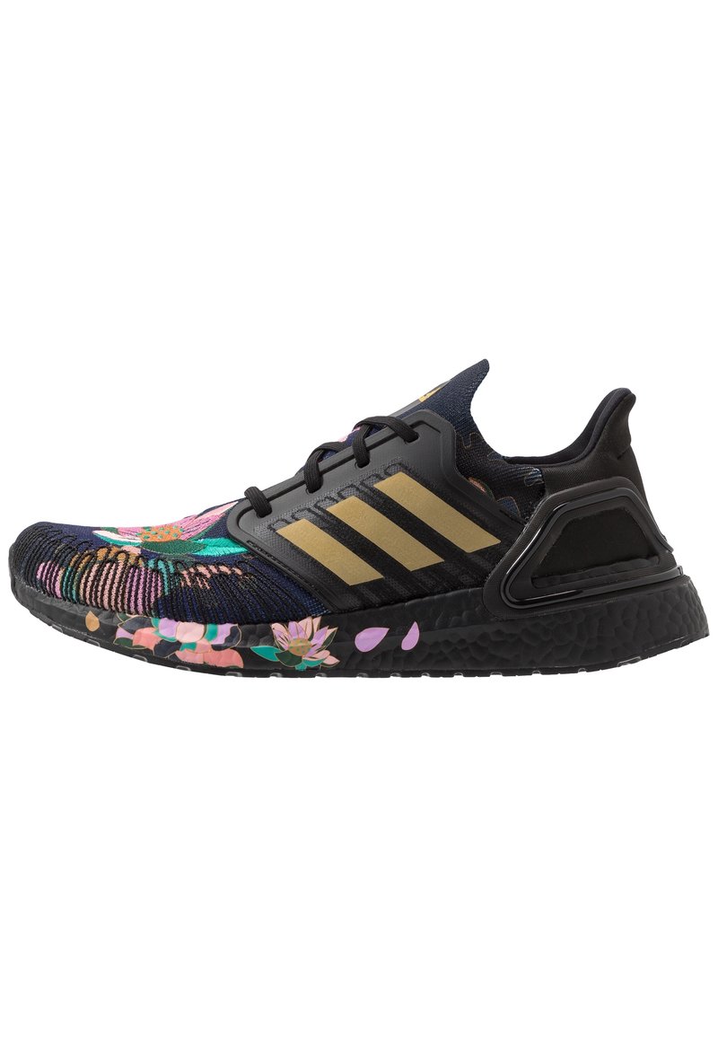 Zapatilla deportiva negra con un upper de tejido de punto con patrón floral, rayas doradas y suela texturizada. Presenta una mediasuela acolchada y detalles de malla.