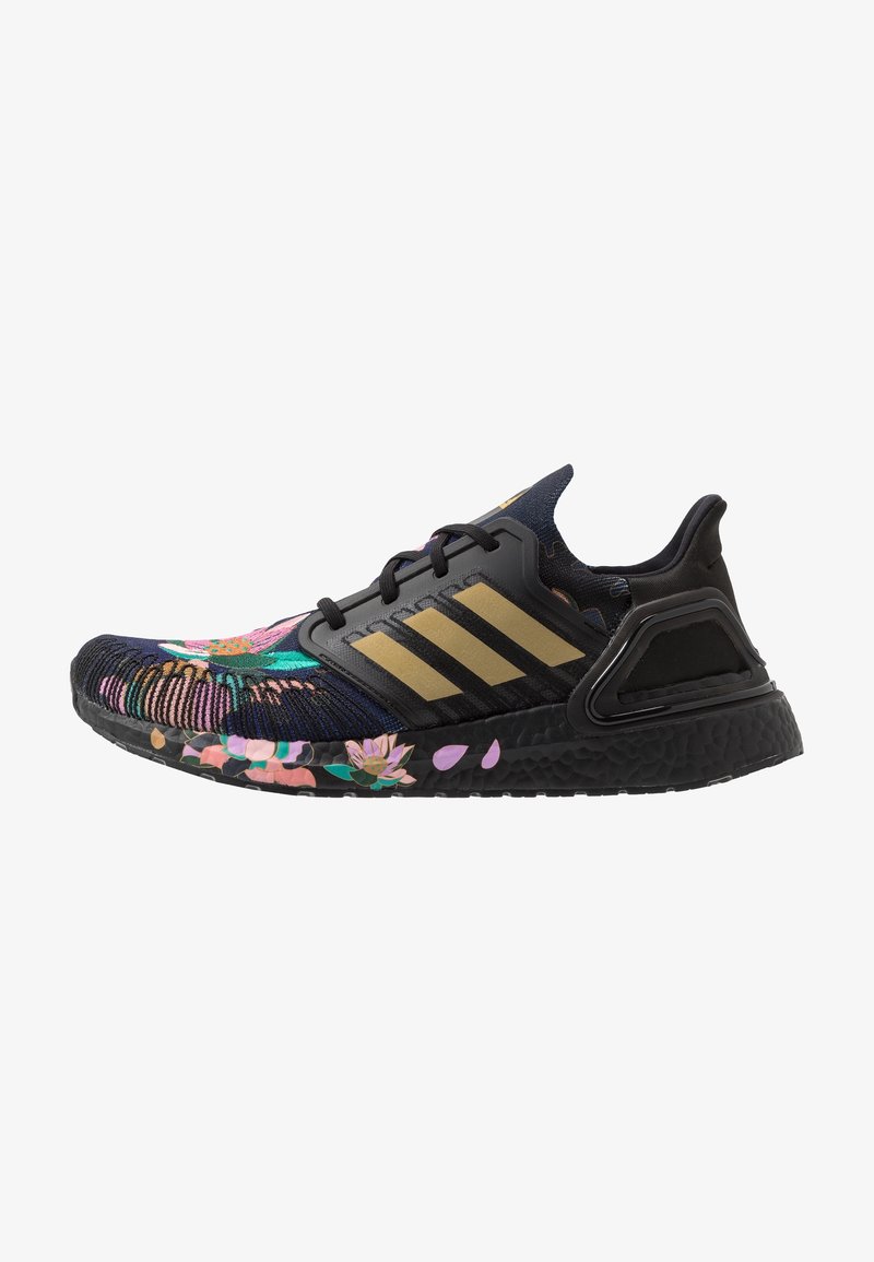 Zapatilla deportiva negra con un upper de tejido de punto con patrón floral, rayas doradas y suela texturizada. Presenta una mediasuela acolchada y detalles de malla.