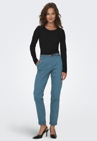 Melna ribota garām piedurknēm augšdaļa, kas apvienota ar tirkīza krāsas pieguļošām biksēm ar svītrainu jostu, papildināta ar melnām augstpapēžu kurpēm.