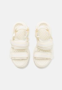 Sandalias blancas con dos correas ajustables de Velcro, plantilla texturizada y un diseño elegante y redondeado. Suelas de goma para un buen agarre y comodidad.