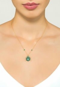 Guldhalsband med en grön skalbagge-pendant och två sm�å gröna detaljer. Skalbaggen har en texturerad design som visar på intrikata detaljer.