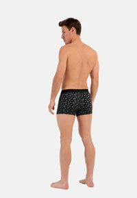 Schwarze Boxershorts mit einem bunten Blumenmuster, figurbetontem Design und elastischem Bund. Modell von hinten gezeigt, barfuß.