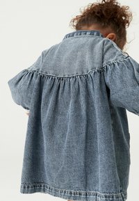 Jeansjacke in Hellblau mit einem gefältelten Design an den Ärmeln und am Rücken, weicher Textur und klassischem Kragen.