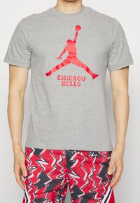 Camiseta de algodón gris con un gran gráfico rojo de "Jumpman" y el texto "CHICAGO BULLS" debajo. Diseño clásico de cuello redondo.