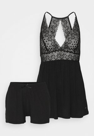 Black sleepwear set featuring a lace-trimmed top with a deep V-neck and elastic waist shorts. Soft fabric, relaxed fit, and minimal accents.