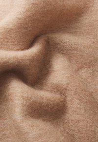 Material gros, moale, de culoare maro deschis, cu o textură pufoasă, prezentând variații subtile de culoare și o suprafață denivelat�ă, cu cute.