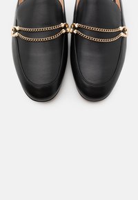 Svarta läder loafers med en mjuk textur, prydda med en guldkedja över foten. Klassisk form med minimala sömnadsdetaljer.