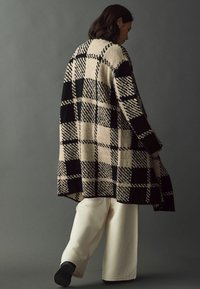 Beige og sort oversized ternet cardigan med en blød tekstur, der har en lang længde og sænkede skuldre, parret med cremede vide bukser.