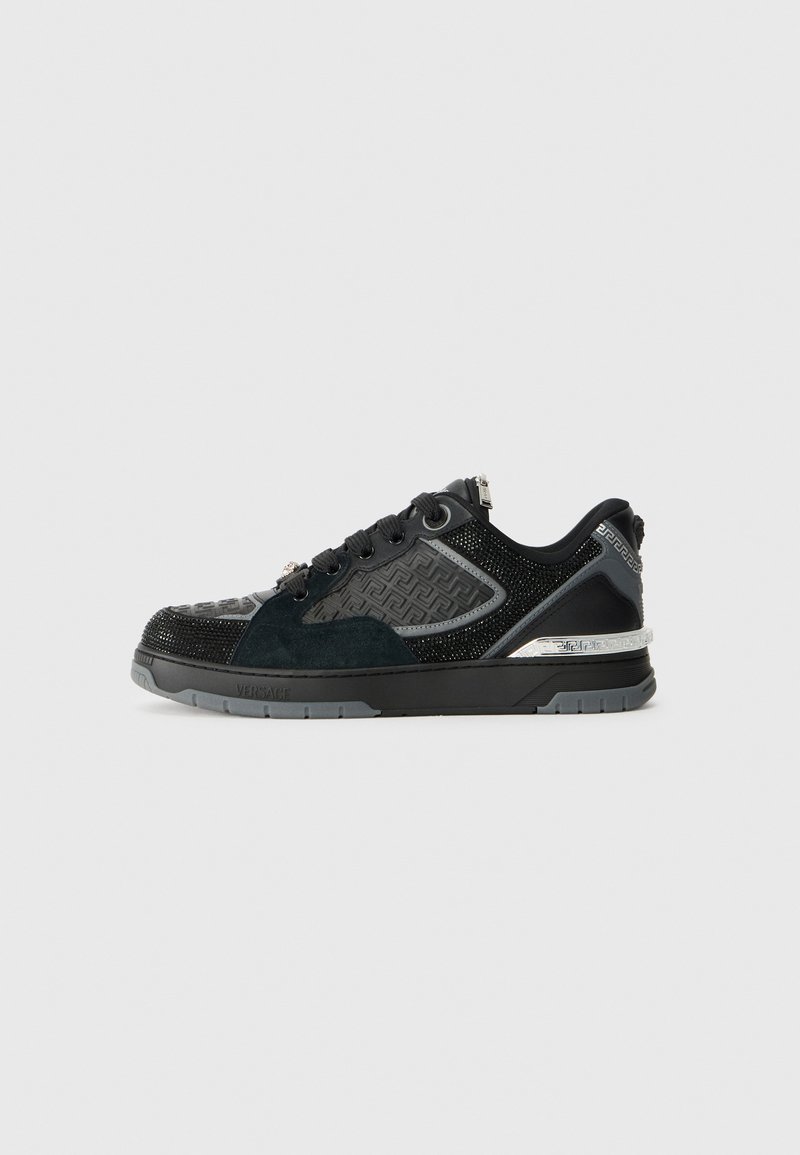 Black athletic shoe with mixed materials including mesh and suede, featuring a textured pattern and metallic accents on the heel and side.
