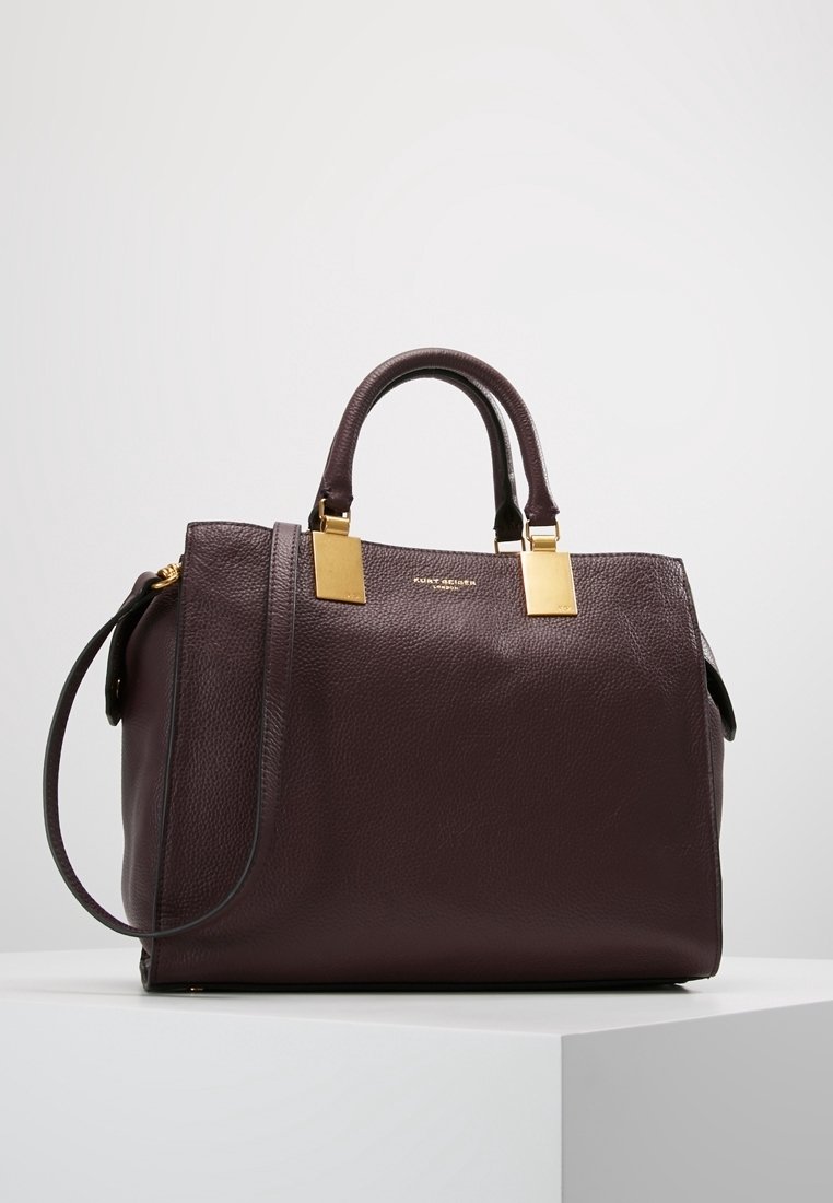 Donker bordeaux lederen handtas met een gestructureerde afwerking, gouden hardware-accenten, dubbele handvatten aan de bovenkant en een afneembare schouderriem.
