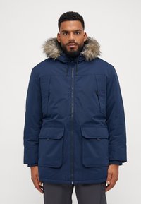 Parka aislante de color azul marino con capucha forrada de pelaje sintético, dos bolsillos frontales, cierre de cremallera y cordones elásticos en la capucha para ajuste.