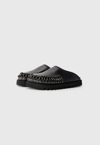 Chaussures noires à enfiler avec des semelles épaisses à nervures et des détails en chaîne en métal cousus le long des bords avant.