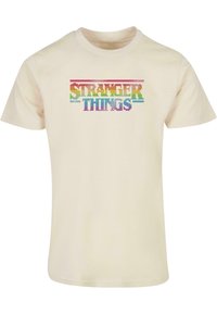 Krémové tričko s krátkým rukávem s barevným nápisem "STRANGER THINGS" v blokovém písmu přes hruď. Materiál: bavlna.