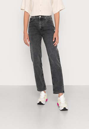 Person, der bærer sorte højtaljede jeans med lige ben, cremefarvet kortærmet skjorte med knapper og hvide sneakers med pink accenter.