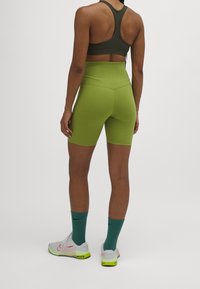 Sostén deportivo verde oliva y pantalones cortos de bicicleta de talle alto a juego, tela texturizada, combinados con zapatos blancos y neón y calcetas turquesa.