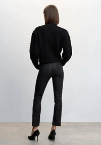 Černý pletený svetr s texturovanými balónovými rukávy, zkombinovaný s úzkými černými kalhotami a černými lodičkami na vysokém podpatku. Zadní pohled na neutrálním pozadí.
