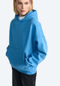 Sudadera con capucha de color azul cielo, con un bolsillo frontal, corte holgado y puños y dobladillo acanalados. Tejido suave con un sutil acento de logo cerca del dobladillo.