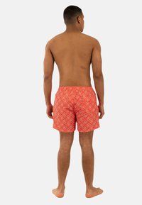 Pantaloni da nuoto rossi con un motivo geometrico bianco, lunghezza sopra il ginocchio, cintura elastica e tessuto leggero.