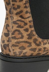 Bottines en suède à imprimé léopard avec un panneau latéral élastique noir et une épaisse semelle plateforme noire. Gros plan sur le matériau et les détails de conception.