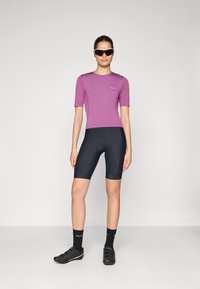 Haut court violet, shorts de cyclisme noirs, chaussures de cyclisme noires et chaussettes noires. Tissu lisse, design ajusté et détail du logo sur le shirt.