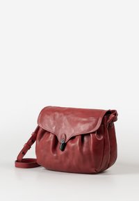 Rote Leder-Umhängetasche mit Klappenverschluss, gerafftem Boden, verstellbarem Tragegurt und einem kleinen schwarzen Hardwaredetail.
