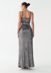 Metalen avondjurk met pailletten, spaghettibandjes, een getailleerd lijfje en een vloeiende zoom, met een verloop van zilveren naar zwarte tinten.