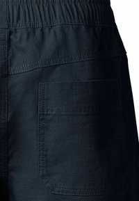 Tissu bleu marine foncé avec une grande poche carrée à l'arrière et des coutures détaillées, montrant un matériau tissé texturé en gros plan.