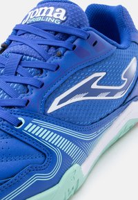 Niebieski sportowy but Joma Dribling z teksturowaną siateczką, sznurowanym zapięciem, białym logo i detalem podeszwy w jasnozielonym kolorze.