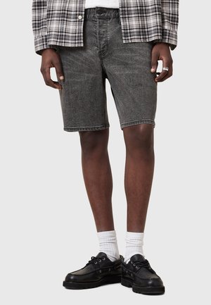 Black denim shorts with textured fabric, straight fit, and five-pocket design. Paired with black shoes and white socks. Plaid shirt on top.