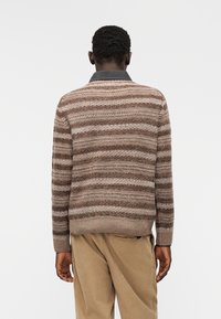 Pletený svetr s hnědod béžovým pruhovaným vzorem, s tmavým límcem, žebrovanými manžetami a texturovanými detaily na látce.