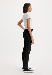 Witte, gestructureerde top met korte mouwen, gecombineerd met zwarte skinny jeans en zwarte high-top sneakers, weergegeven in een zijaanzicht.